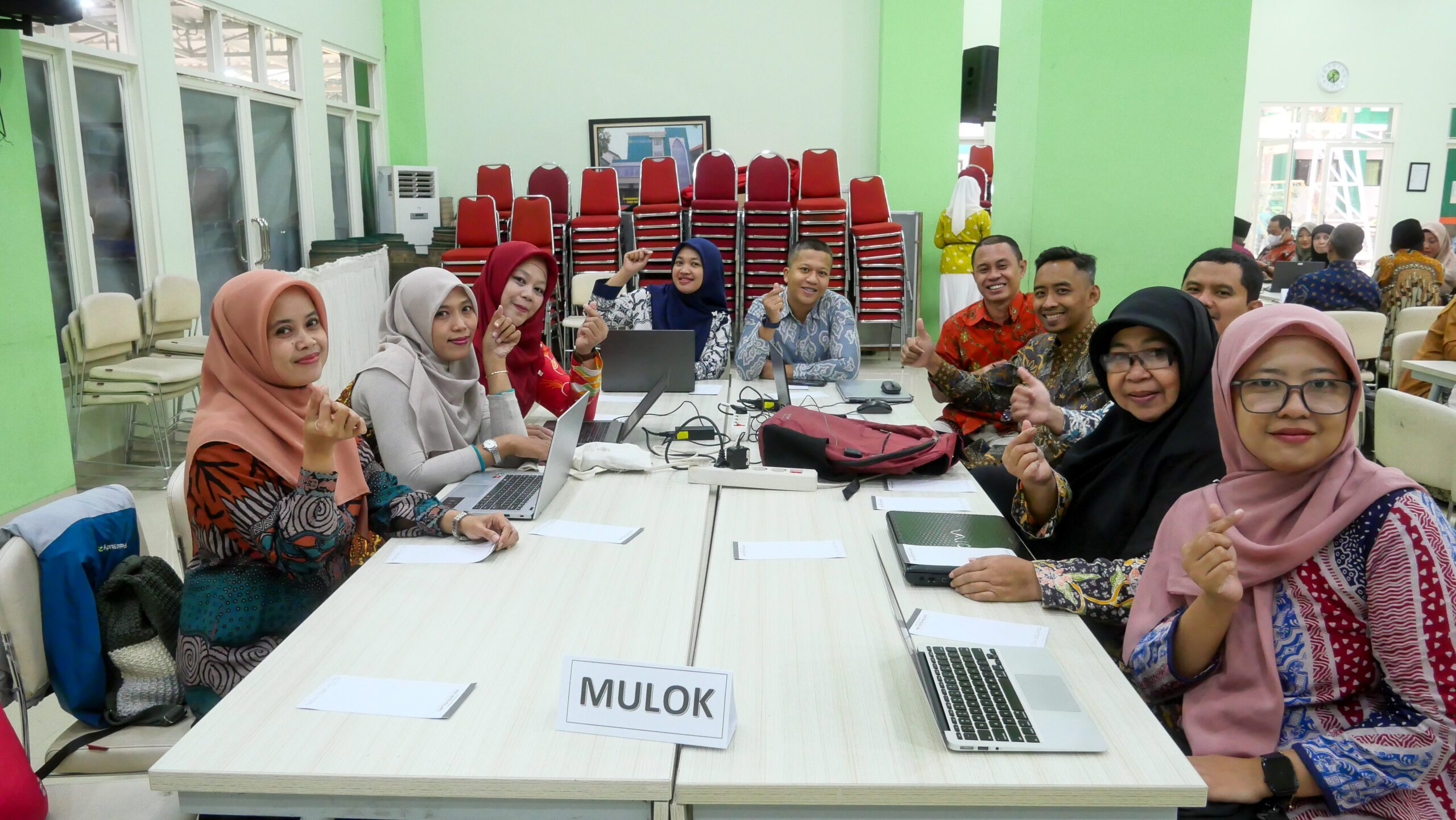 Sekelompok guru berfoto bersama dengan laptop di meja saat pelatihan